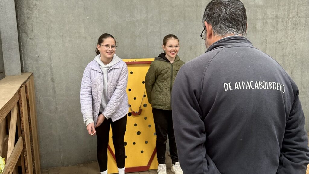 Twee kinderen doen mee aan een boerderijspel tijdens het dagkamp, begeleid door boer John